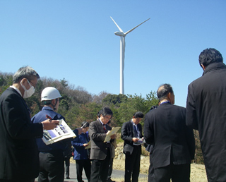 風力発電設備の前で説明を受ける見学者